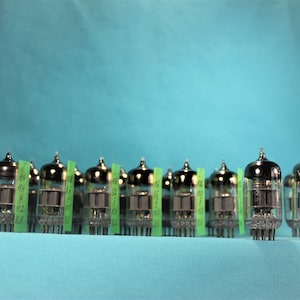 Puede incluir: Una fila de 14 tubos de vacío plateados con etiquetas verdes sobre un fondo azul claro.