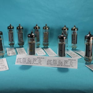 May include: Eight silver vacuum tubes with black caps and metal pins. Each tube has a paper label with text and numbers. The labels are dated 2023-03-03.