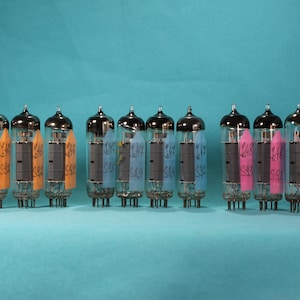 May include: A row of 12 silver vacuum tubes with colored labels. The labels have handwritten text on them, including "146 S82" and "147 S84".