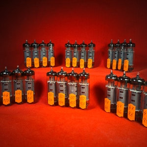 May include: A collection of vintage vacuum tubes, some with orange labels, arranged on a red surface. The labels have numbers on them, including 48, 49, 50, 64, 47, 44, and 99.