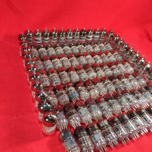 May include: A large collection of vintage vacuum tubes, arranged in a grid pattern on a red surface. The tubes are made of glass and metal, and have a silver finish.