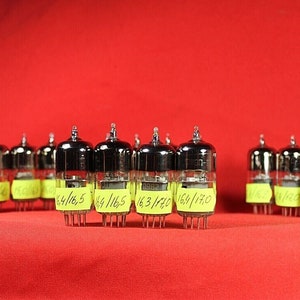 May include: A group of 12 vintage vacuum tubes with silver caps and glass bodies. Each tube has a yellow sticker with handwritten numbers and fractions, such as 150/165, 64/16.5, and 16.3/140.