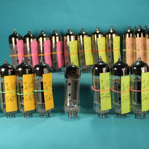 Peut inclure: Une collection de 20 tubes à vide vintage, certains avec des étiquettes jaunes et vertes, disposés en rangées sur une surface bleue. Les étiquettes portent des inscriptions manuscrites, notamment "M-45" et "S-60".