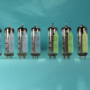 May include: A row of seven vacuum tubes with silver tops and glass bodies. Each tube has a label with numbers and letters. The tubes are on a teal surface.