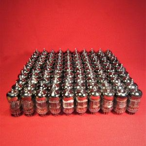 Puede incluir: Un gran grupo de tubos de vacío plateados, dispuestos en una cuadrícula sobre un fondo rojo. Los tubos son todos idénticos y tienen un cuerpo de vidrio transparente con una base de metal.