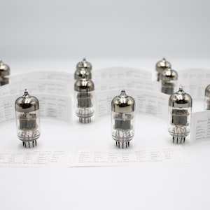 May include: Several vacuum tubes with silver caps and transparent glass bodies, displayed with data sheets. The tubes have multiple pins at the base. The background is plain white.
