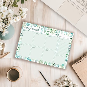 Peut inclure: Un bloc-notes planificateur hebdomadaire avec un motif botanique. Le bloc-notes présente un fond vert clair avec des sections pour chaque jour de la semaine, une liste de tâches et des notes. La bordure est ornée de feuilles vertes et bleues.