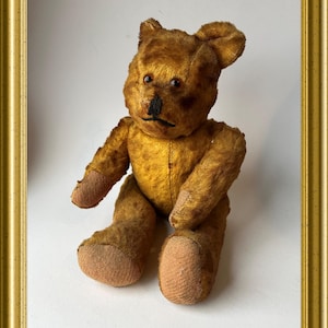 Op de afbeelding: Een vintage bruine teddybeer met knoopjesogen en een gestikte neus, zittend op een witte achtergrond.