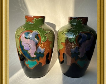 May include: Two ceramic vases with a black background and colorful floral designs. The vases have a green, orange, blue, and purple color scheme.