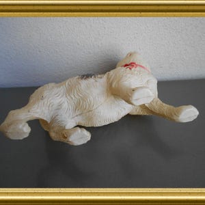 May include: A vintage white and tan dog figurine with a red ribbon around its neck. The dog is lying on its back with its paws in the air. The figurine has a textured, fur-like appearance.