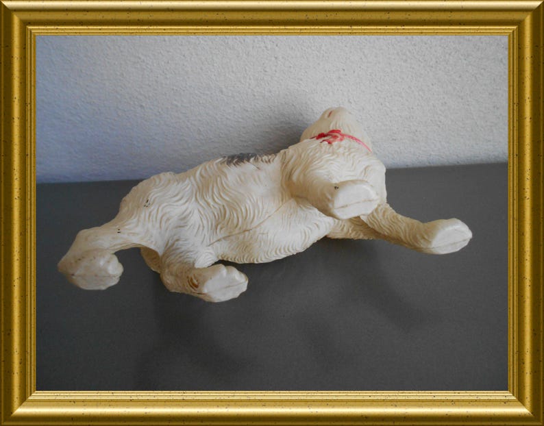 May include: A vintage white and tan dog figurine with a red ribbon around its neck. The dog is lying on its back with its paws in the air. The figurine has a textured, fur-like appearance.
