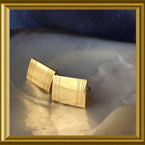 Könnte beinhalten: Ein Paar goldene Manschettenknöpfe in rechteckiger Form mit einem gerillten Design.