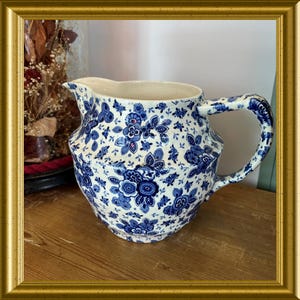 以下が含まれることがあります： 白地に青い花柄のヴィンテージセラミックピッチャー。ピッチャーは、注ぎやすいように湾曲したハンドルと注ぎ口が付いています。花柄のデザインには、さまざまな花や葉の形が含まれています。