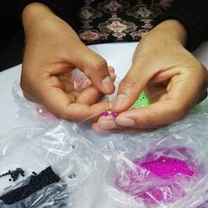 May include: A person is stringing beads. There are bags of black, green, and pink beads.