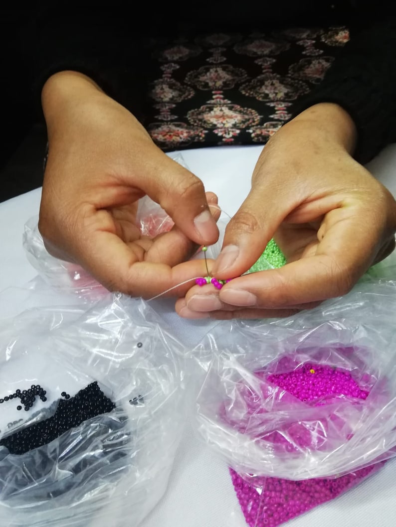 May include: A person is stringing beads. There are bags of black, green, and pink beads.