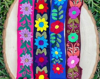 May include: Four embroidered fabric strips with floral designs. The strips are in pink, navy blue, blue, and maroon. The designs feature flowers, leaves, and vines.