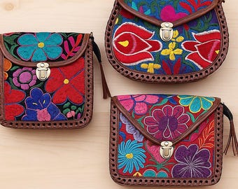 May include: Three handbags featuring vibrant floral embroidery in shades of red, blue, purple, and yellow. Each bag has a brown leather-like trim with decorative stitching, a fold-over flap, and a silver-toned metal push-lock closure.