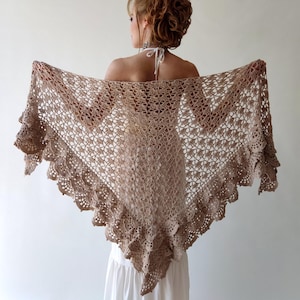 May include: A crocheted shawl with a delicate lace pattern and a ruffled edge. The shawl is a light brown color and is made of a soft, lightweight yarn.