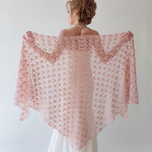 Puede incluir: Un chal rosa claro, de tejido abierto, con un estampado floral. El chal se sostiene abierto, mostrando su delicado dise&ntilde;o y textura. La prenda parece hecha a mano, adecuada para una ocasi&oacute;n especial.