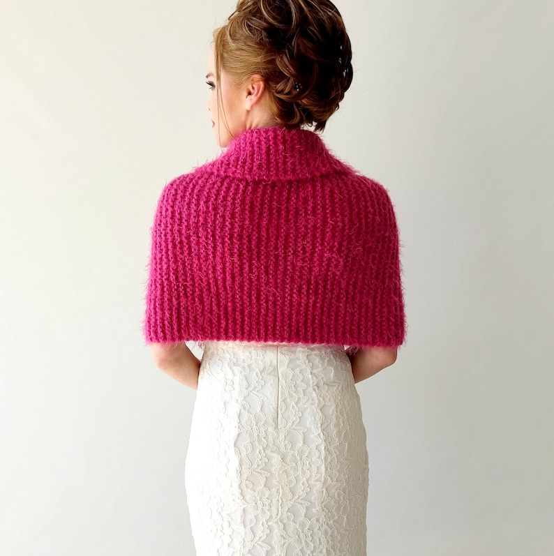 K&ouml;nnte beinhalten: Ein rosa, flauschiger Strick-Schal mit hohem Kragen. Der Schal ist aus weichem, flauschigem Garn gefertigt und hat ein schlichtes, elegantes Design.