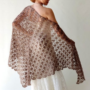 Könnte beinhalten: Ein braunes Häkeltuch mit einem zarten Lochmuster. Das Tuch ist über die Schultern einer Person gelegt und wird als Umhang getragen.