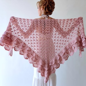 May include: A dusty rose crochet shawl with a delicate floral pattern and scalloped edges. The shawl is draped over the shoulders, showcasing its intricate design and texture. The shawl's color is a soft, muted pink.