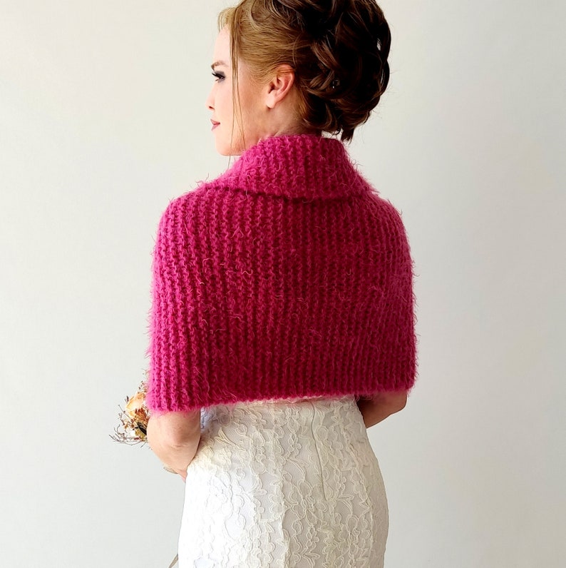 K&ouml;nnte beinhalten: Eine rosa gestrickte Schulterw&auml;rmer mit hohem Kragen. Die Schulterw&auml;rmer sind aus einem weichen, flauschigen Garn gefertigt und haben ein schlichtes, elegantes Design.