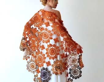 May include: A crocheted shawl in shades of orange, brown, and beige with a delicate floral pattern. The shawl is draped over a white dress.