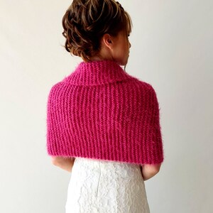 K&ouml;nnte beinhalten: Eine rosa gestrickte Schulterw&auml;rmer mit Rollkragen. Die Schulterw&auml;rmer sind aus einem weichen, flauschigen Garn gefertigt und haben eine lockere, flie&szlig;ende Passform.