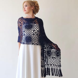 Peut inclure: Un châle en crochet bleu marine avec un motif floral et des franges. Le châle est drapé sur une robe blanche. Le tissage ouvert du châle est visible, et le motif floral est répété dans toute la conception.