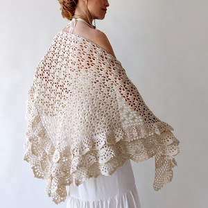 May include: A crocheted shawl with a delicate, lacy pattern and a scalloped edge. The shawl is made in a cream color and is draped over a person's shoulders.