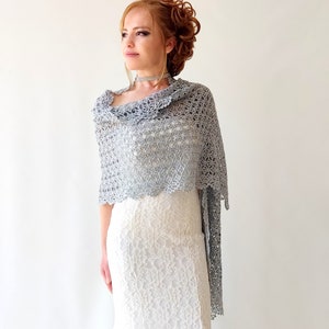 May include: A silver crochet shawl with a delicate floral pattern. The shawl is draped over a white lace dress.