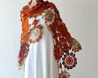 May include: A crocheted shawl in shades of orange, brown, and white. The shawl is made of delicate lace and features a variety of floral motifs.