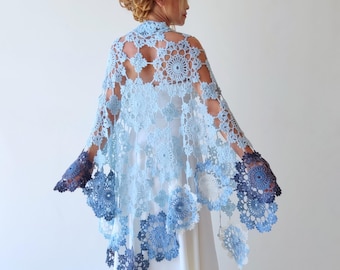 Puede incluir: Un chal de ganchillo azul claro con un degradado de color de azul claro a azul oscuro. El chal está hecho de delicadas flores de ganchillo y tiene un borde festoneado.
