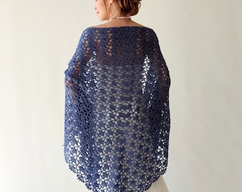 May include: A blue crocheted shawl with a delicate floral pattern. The shawl is draped over a white dress.