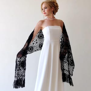 May include: A black crochet shawl with a floral pattern and fringe. The shawl is draped over the shoulders of a person wearing a white strapless dress.
