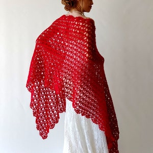 May include: A red crochet shawl with a delicate floral pattern. The shawl is draped over a white dress.