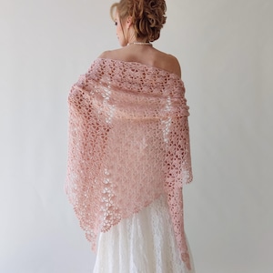 Puede incluir: Un chal rosa claro, de tejido abierto, con un estampado floral. El chal est&aacute; drapeado sobre los hombros, revelando un vestido blanco. El dise&ntilde;o delicado y el color suave crean un aspecto elegante y rom&aacute;ntico, adecuado para ocasiones especiales.