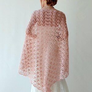 Puede incluir: Un chal de ganchillo rosa claro de tejido abierto. El chal est&aacute; drapeado sobre los hombros, mostrando un delicado estampado floral. El intrincado dise&ntilde;o y el color suave crean una est&eacute;tica elegante y aireada, adecuada para ocasiones especiales o para a&ntilde;adir un toque de encanto vintage a un atuendo.