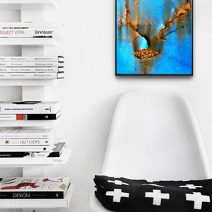 Puede incluir: Un primer plano de una pintura abstracta azul y naranja con un marco negro. La pintura est&aacute; colgada en una pared blanca sobre una silla blanca con un coj&iacute;n blanco y negro.
