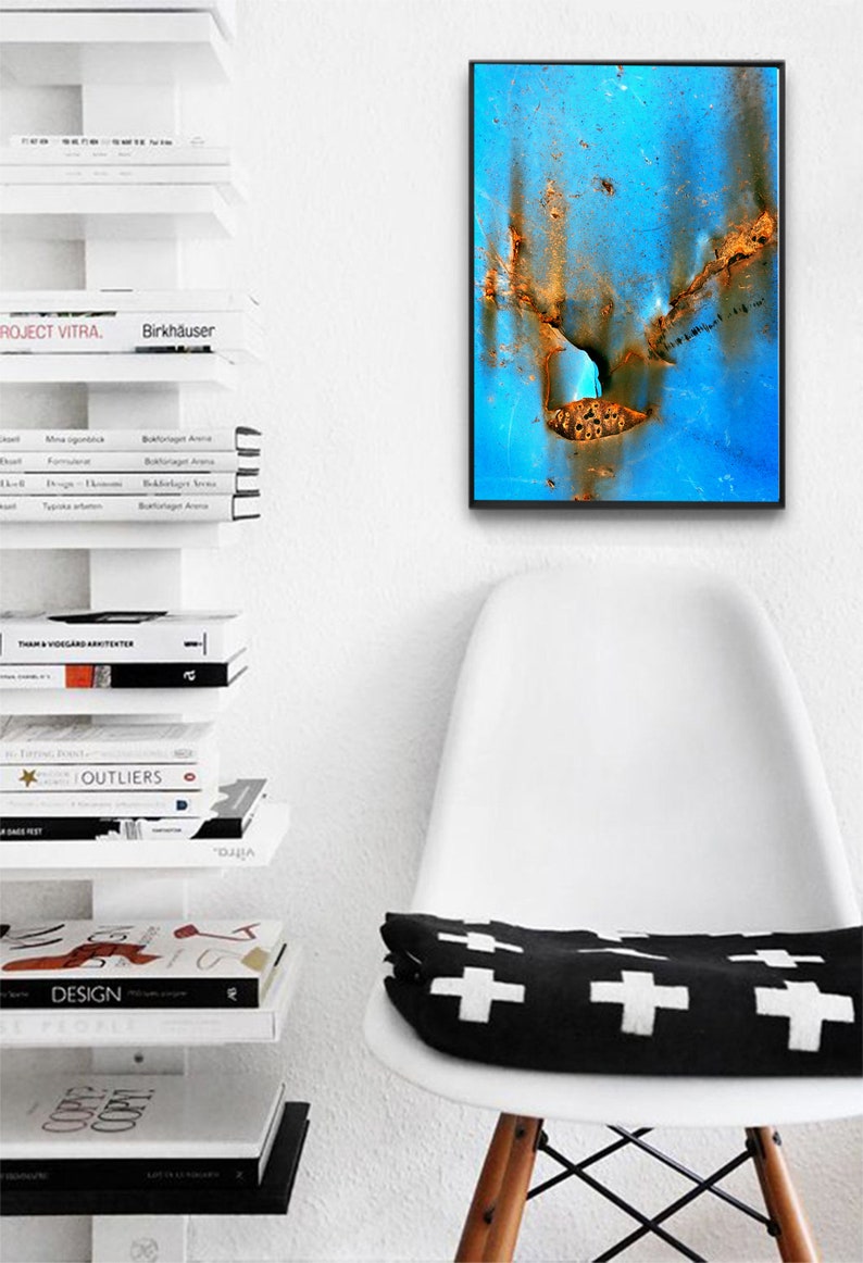 Puede incluir: Un primer plano de una pintura abstracta azul y naranja con un marco negro. La pintura est&aacute; colgada en una pared blanca sobre una silla blanca con un coj&iacute;n blanco y negro.