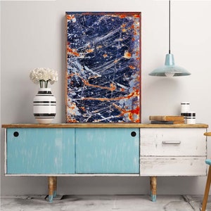 Pode incluir: Um arm&aacute;rio azul, branco e madeira com duas portas e uma gaveta. O arm&aacute;rio tem um acabamento desgastado e &eacute; decorado com um vaso preto e branco com flores brancas. Uma pintura abstrata emoldurada com uma combina&ccedil;&atilde;o de cores azul, laranja e branco est&aacute; pendurada acima do arm&aacute;rio.