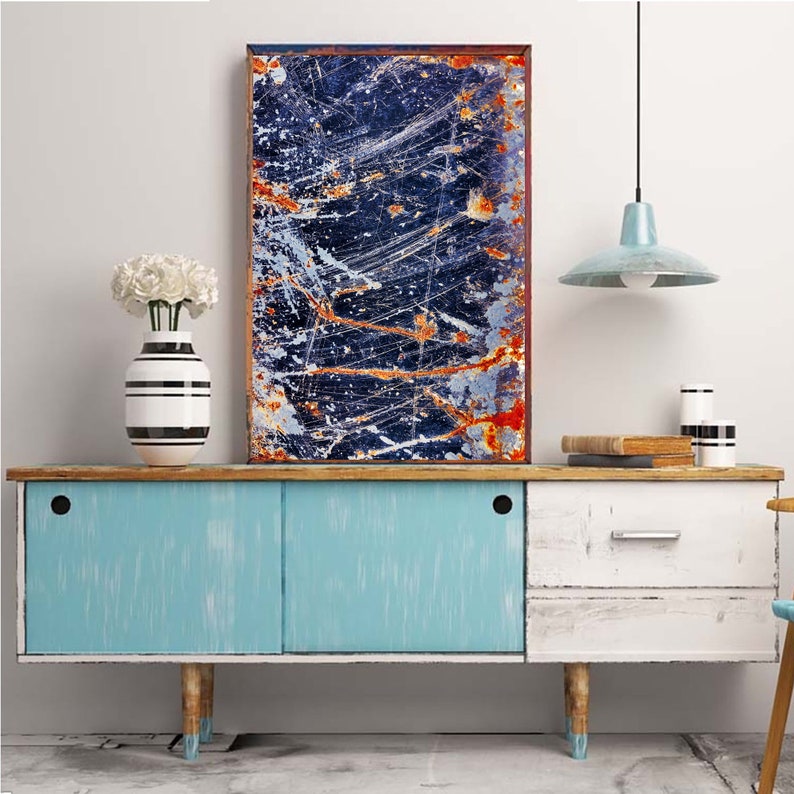 Pode incluir: Um arm&aacute;rio azul, branco e madeira com duas portas e uma gaveta. O arm&aacute;rio tem um acabamento desgastado e &eacute; decorado com um vaso preto e branco com flores brancas. Uma pintura abstrata emoldurada com uma combina&ccedil;&atilde;o de cores azul, laranja e branco est&aacute; pendurada acima do arm&aacute;rio.