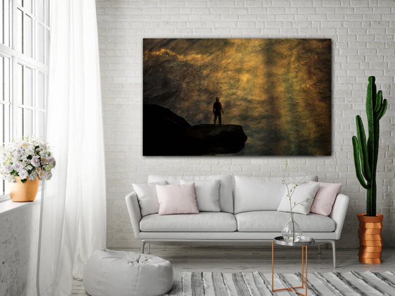 K&ouml;nnte beinhalten: Eine Silhouette einer Person, die auf einem felsigen Vorsprung steht, vor dem Hintergrund eines goldenen, strukturierten Himmels.