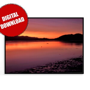 Puede incluir: Una puesta de sol escénica sobre un cuerpo de agua tranquilo con una costa distante. El cielo es una mezcla vibrante de tonos naranja, rosa y morado, que se reflejan en la superficie del agua.