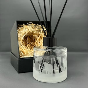 May include: A frosted glass diffuser bottle with a black lid and reeds. The bottle has an etched design of a Highland cow in a field. The diffuser is packaged in a black box with shredded paper.