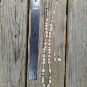May include: A necklace and earring set featuring a variety of light-colored, polished gemstones. The necklace includes a square pendant and is approximately 12 inches long. The earrings are small and dangle. The set is displayed on a wooden surface.