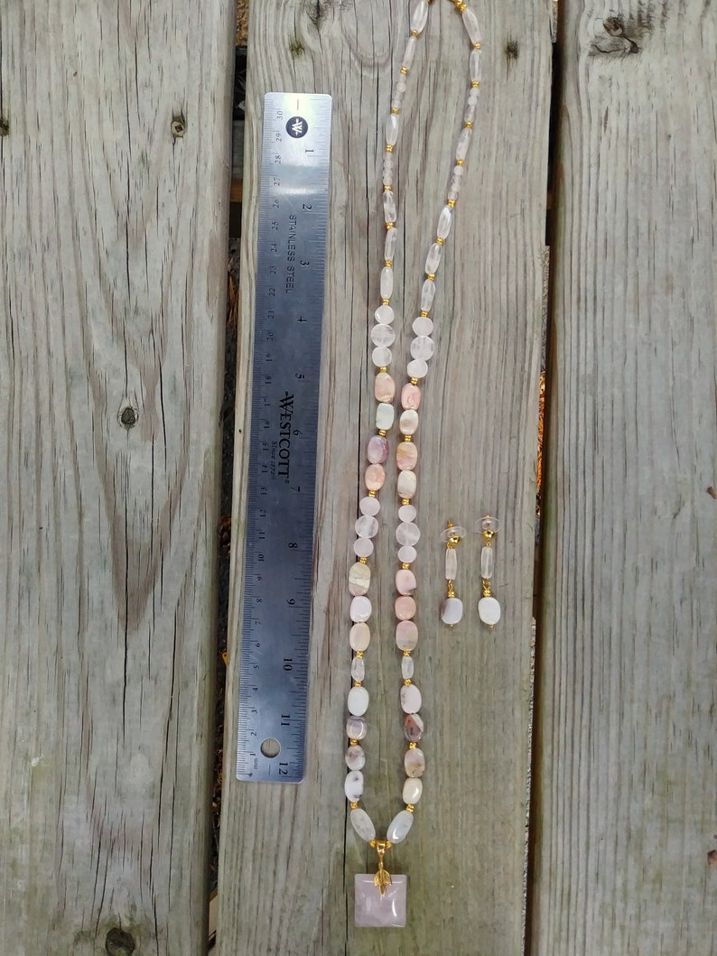May include: A necklace and earring set featuring a variety of light-colored, polished gemstones. The necklace includes a square pendant and is approximately 12 inches long. The earrings are small and dangle. The set is displayed on a wooden surface.