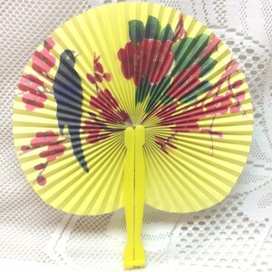 May include: A yellow folding fan with a black bird and red flowers painted on it. The fan is closed and has a yellow handle.