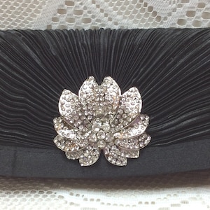 May include: A black satin clutch with a large, silver, rhinestone flower embellishment.